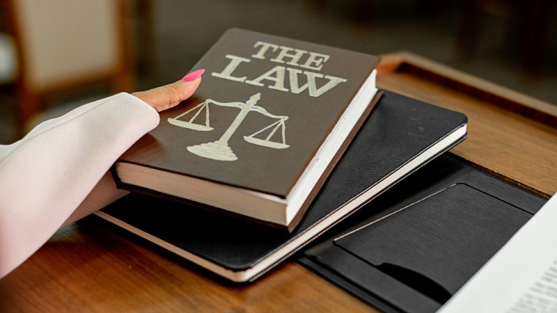 Closeup image of a law book titled 'The Law' on a wooden desk with scales of justice., tags: der - pexel